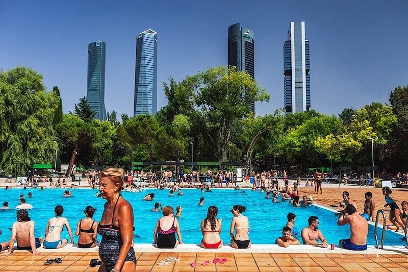 Bañistas en la piscina municipal de Vicente del Bosque, en Madrid, con el perfil de las Cuatro Torres al fondo.