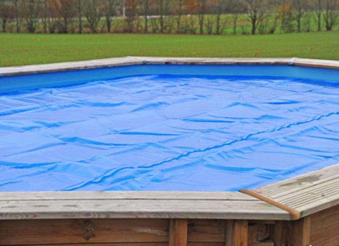 Imagen de piscina ovalada de madera con una cubierta azul
