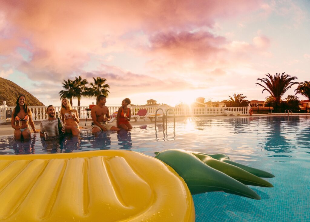 Happy friends having fun in pool party at sunset